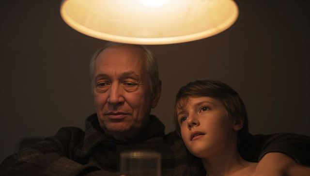 Grandfather and Grandson Sharing Cozy Evening on Sofa Under Warm Pendant Lamp, Tender Family Moment