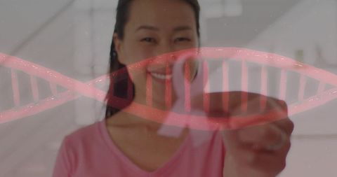 Smiling korean woman reaching across glass panel with red dna helix for genetics research