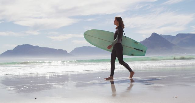 Happy biracial woman walking along beach by the sea carrying surfboard. healthy active lifestyle, close to nature.