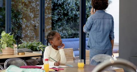 Child doing homework while mother talks on smartphone nearby