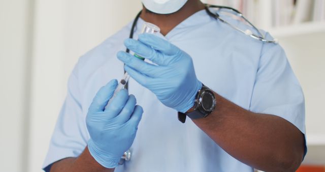 Healthcare professional wearing blue scrubs and gloves, preparing a vaccine injection with a syringe. Ideal for medical websites, articles on vaccination, healthcare promotions, and public health campaigns.