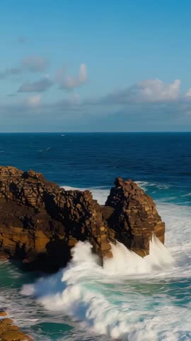Vertical video: Crashing waves smashing rust-colored coastal rock with foamy surf