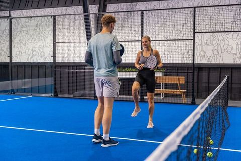 Young adults practicing padel drill on indoor blue court with rackets and net