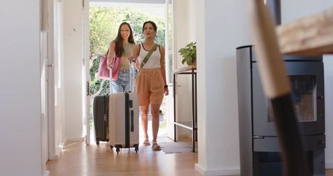 Friends entering vacation rental pulling suitcases and carrying bags into bright foyer