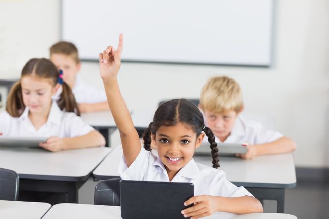 Smiling schoolgirl raising hand in classroom at school