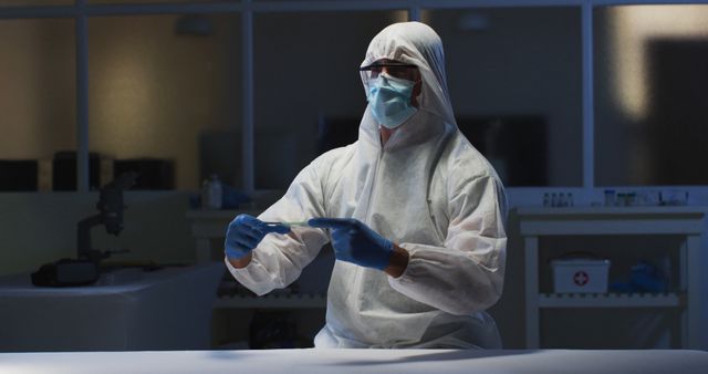 Caucasian male medical worker wearing protective clothing and gloves using handheld interface in lab. healthcare, medical research technology and hygiene during coronavirus covid 19 pandemic.