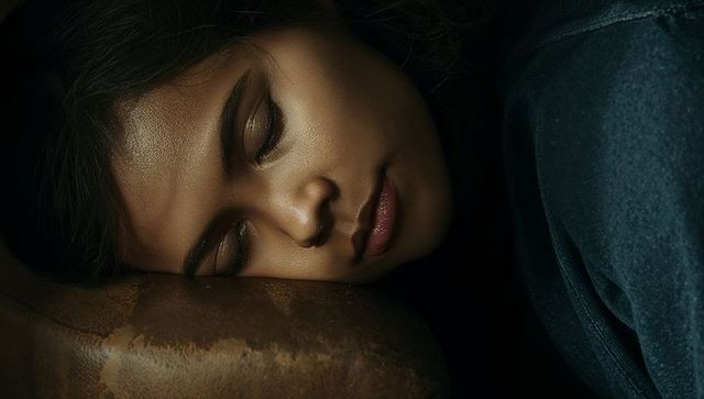 Reclining woman resting head on worn leather armrest in moody dim light, intimate portrait