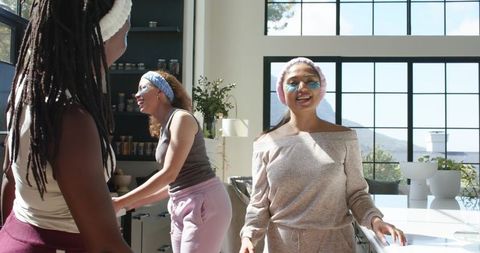 African american women laughing in sunlit modern kitchen wearing loungewear and headbands