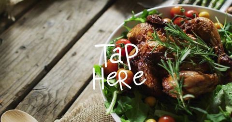 Rustic roast chicken garnished with rosemary on bed of greens and cherry tomatoes