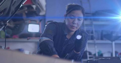 Female Mechanic Inspecting Engine with Flashlight in Auto Repair Shop