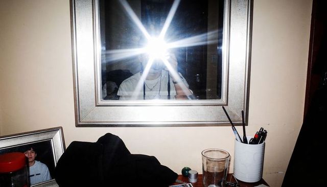 Mirror flash selfie on cluttered dresser with camera reflection, glass, pens and personal items