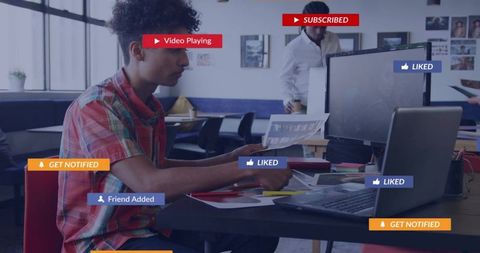 Young man reviewing printouts at laptop with social ui overlays in coworking