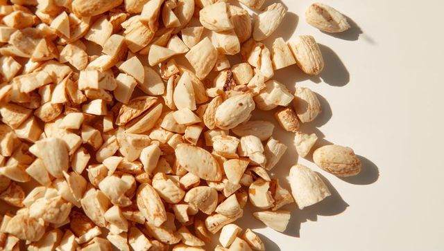 Chopped almonds casting warm shadows on cream surface, close-up flatlay