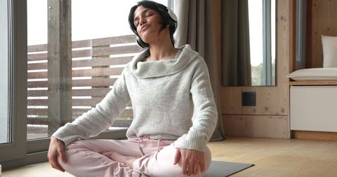 Woman meditating with headphones in cozy wooden cabin