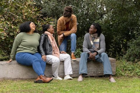 Diverse friends laughing and chatting on wooden bench in park wearing scarves and casual fall style