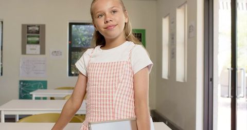 Young student standing and holding tablet in sunlit classroom showing curiosity and calm