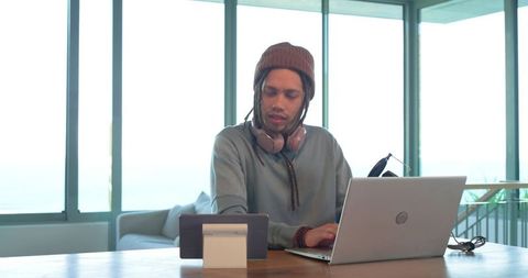 Young man working remote on laptop and tablet with headphones in bright modern home office