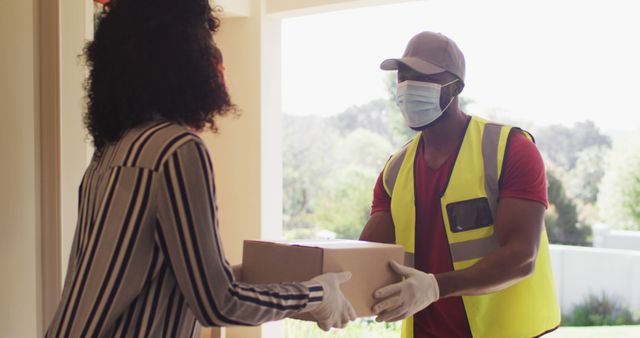 Delivery man wearing face mask delivering package to african american woman wearing face mask at home. social distancing during covid 19 coronavirus quarantine lockdown