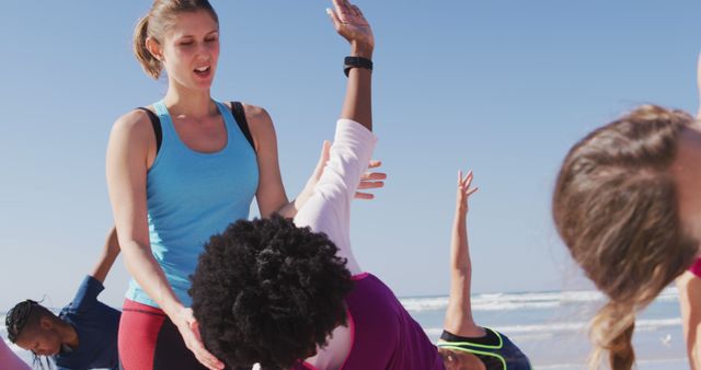 Fitness trainer guiding a diverse group of individuals through yoga exercises outdoors on a sunny beach. This captures the essence of teamwork, healthy lifestyle, and outdoor activities. Ideal for websites or publications related to fitness training, outdoor workouts, beach exercises, and group fitness classes.