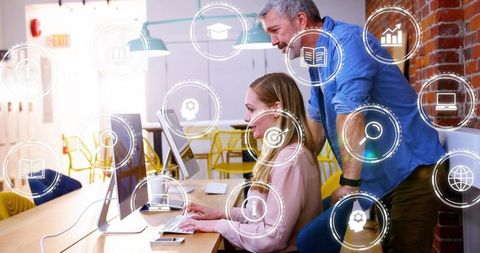 Mentoring midcareer woman at desktop with HUD icons highlighting teamwork and analytics