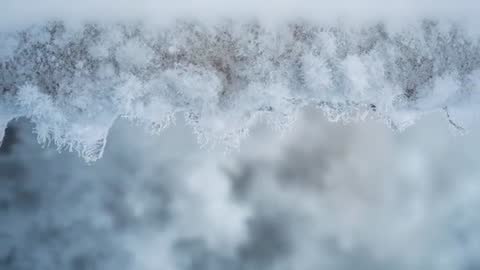 Drifting camera capturing frost-covered railing edge with ice crystals and soft bokeh