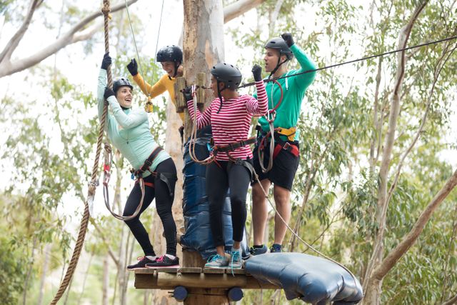 Four friends standing on a platform attached to zip line cables, wearing helmets and safety gear. They appear excited and are preparing for a zip line activity in an outdoor park surrounded by trees. Ideal for use in articles about outdoor adventures, team-building activities, recreational sports, and nature excursions.