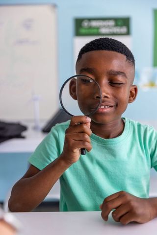African american boy exploring science with magnifying glass in bright classroom