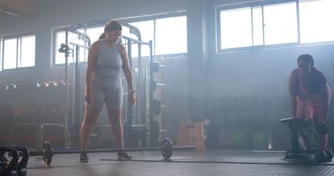 Two women preparing for heavy deadlift in industrial gym, focused strength training