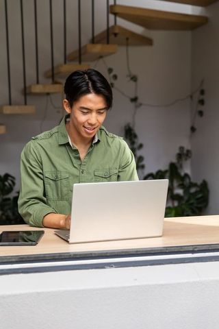 Asian man working on laptop at home counter with modern minimalist interior and plants