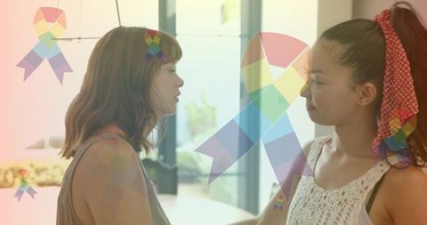 Two women standing face-to-face sharing supportive moment with rainbow ribbon overlay