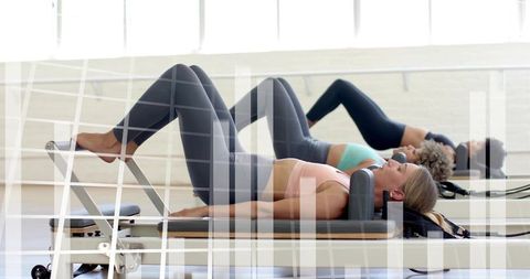 Three women performing pilates reformer leg presses in bright group fitness class