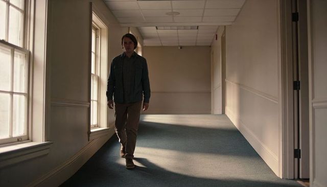 Young man walking down sunlit corridor with sash windows casting long shadows