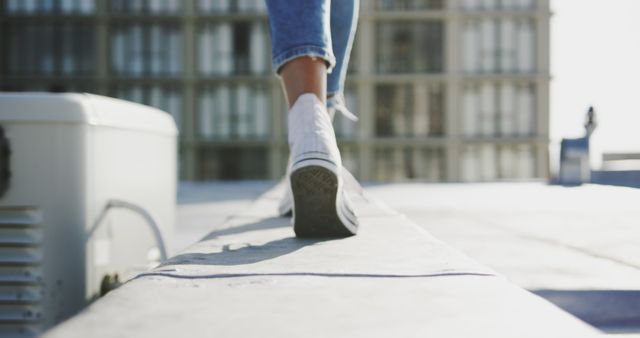 Person walking on a rooftop area, wearing stylish white sneakers and denim jeans. Depicts a carefree urban lifestyle with a focus on casual footwear and city environment. Ideal for use in advertisements, lifestyle blogs, urban-themed campaigns, or fashion promotions related to casual clothing and outdoor activities.