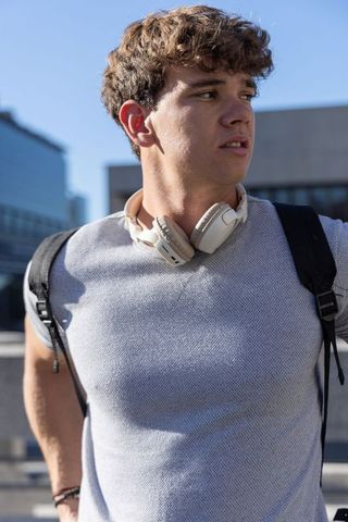 Young man standing on rooftop wearing headphones and backpack looking toward city skyline