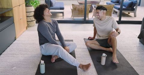 Male Friends Laughing and Stretching on Yoga Mats in Home Environment
