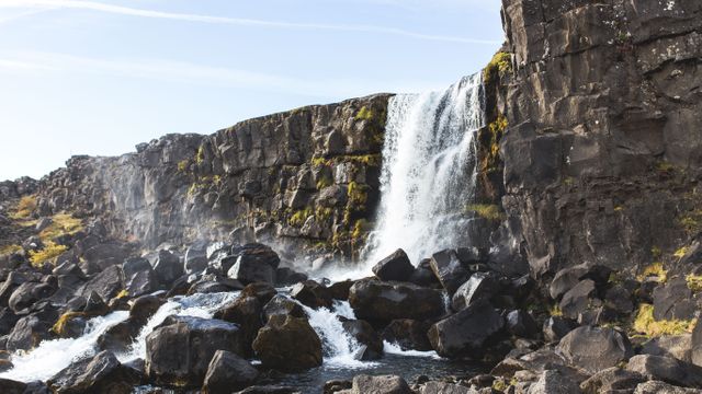 Waterfall cascading over a rugged, rocky cliff with surrounding mossy rocks, ideal for travel blogs, adventure websites, and nature documentaries. Highlights the raw beauty of nature and rugged landscapes, promotes outdoor exploration and nature conservation.