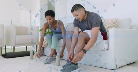 Partners tying running shoes in living room preparing for home workout in activewear