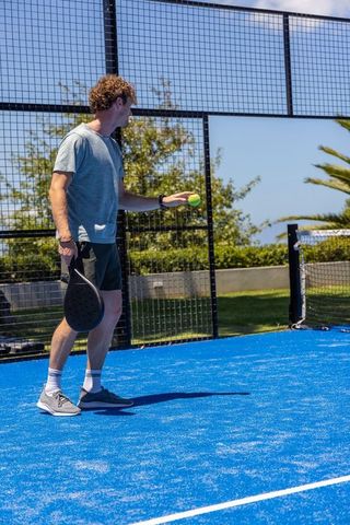 Man holding ball on blue padel court preparing serve under sunny sky