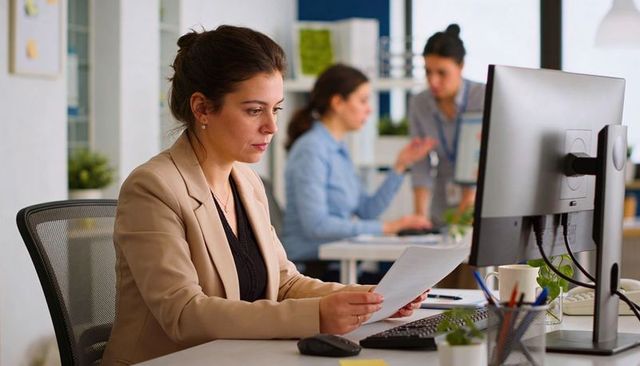 Businesswoman reviewing documents at desk in modern open-plan office with colleagues