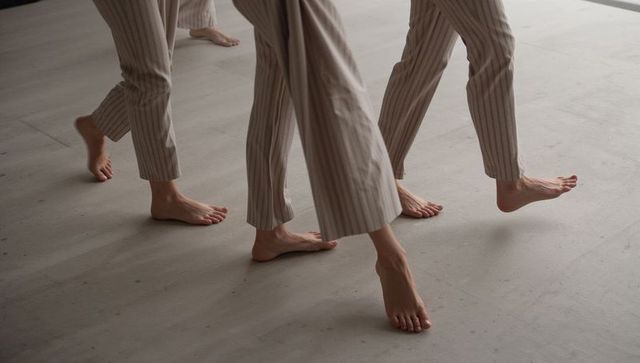 Three barefoot people walking in beige pinstripe cropped trousers on studio floor