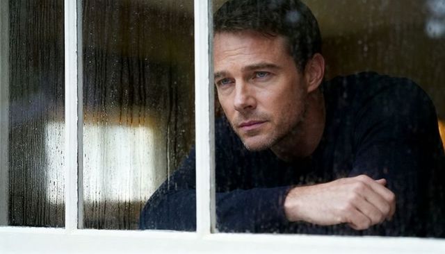 Man gazing through rain-streaked window leaning on sill quiet contemplation