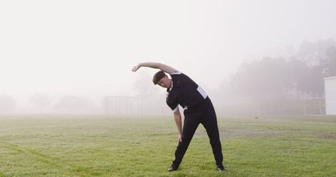 Male Athlete Stretching in Misty Field for Morning Fitness Exercise