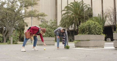 Senior couple reaching for ball and potted plant in urban plaza enjoying outdoor activity