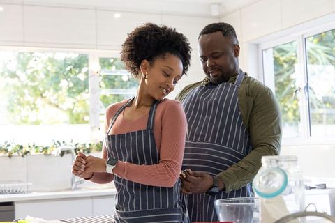African american couple cooking in sunny kitchen, man tying partner apron behind