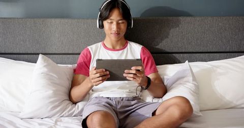 Asian Teen Using Tablet with Headphones Relaxing on Bed
