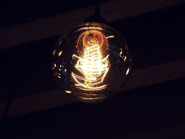 Glowing vintage light bulb with filament glowing against dark background. Can be used in articles or adverts about energy, lighting decor, vintage homes, and electrical concepts. Ideal for adding a warm, retro touch to design projects or illustrating concepts of innovation and ideas.