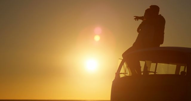 Silhouette of romantic couple sitting on roof of van. Beautiful sunset in background 4k