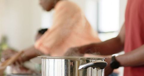 Steaming stainless steel saucepan on stove with family cooking together in kitchen