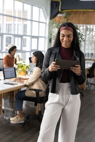 Smiling woman checking tablet in modern coworking space with team and laptops