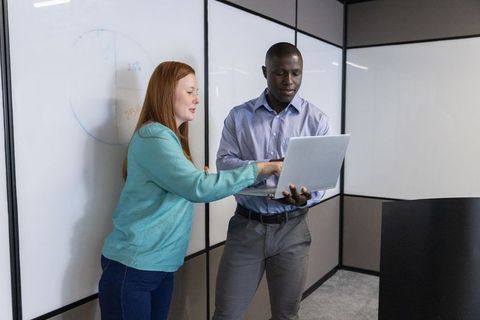Coworkers collaborating on laptop in modern office meeting room